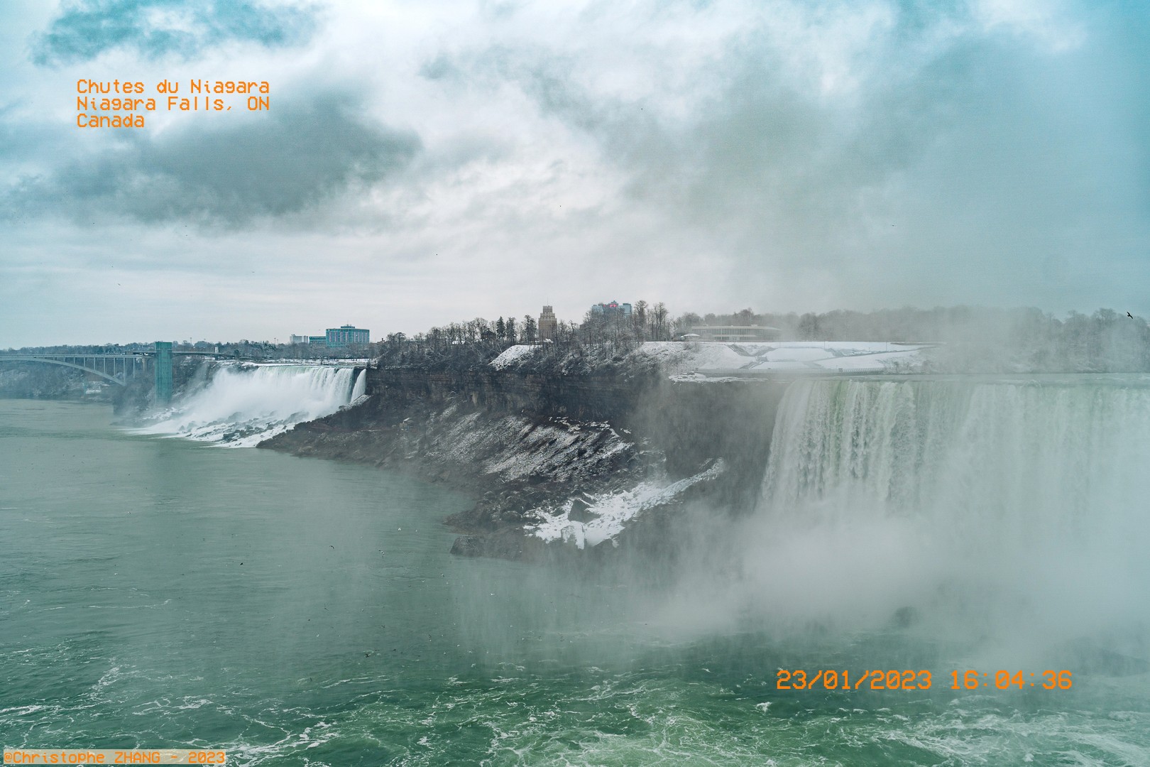 Vue panoramique hivernale des chutes du Niagara, avec brume et rivière verdâtre.