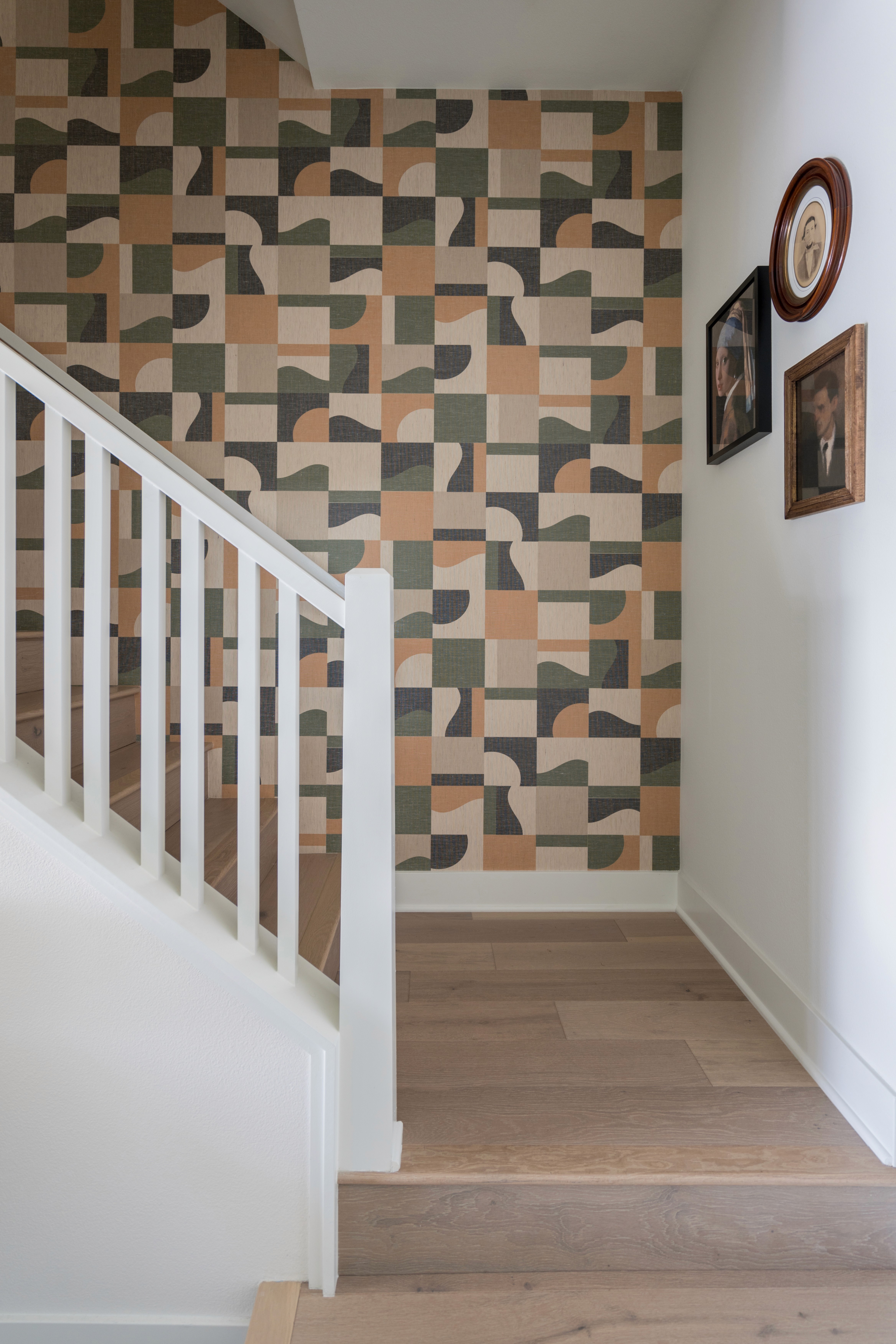 Green, orange, and beige wall paper stairwell, white banister, and light wood flooring