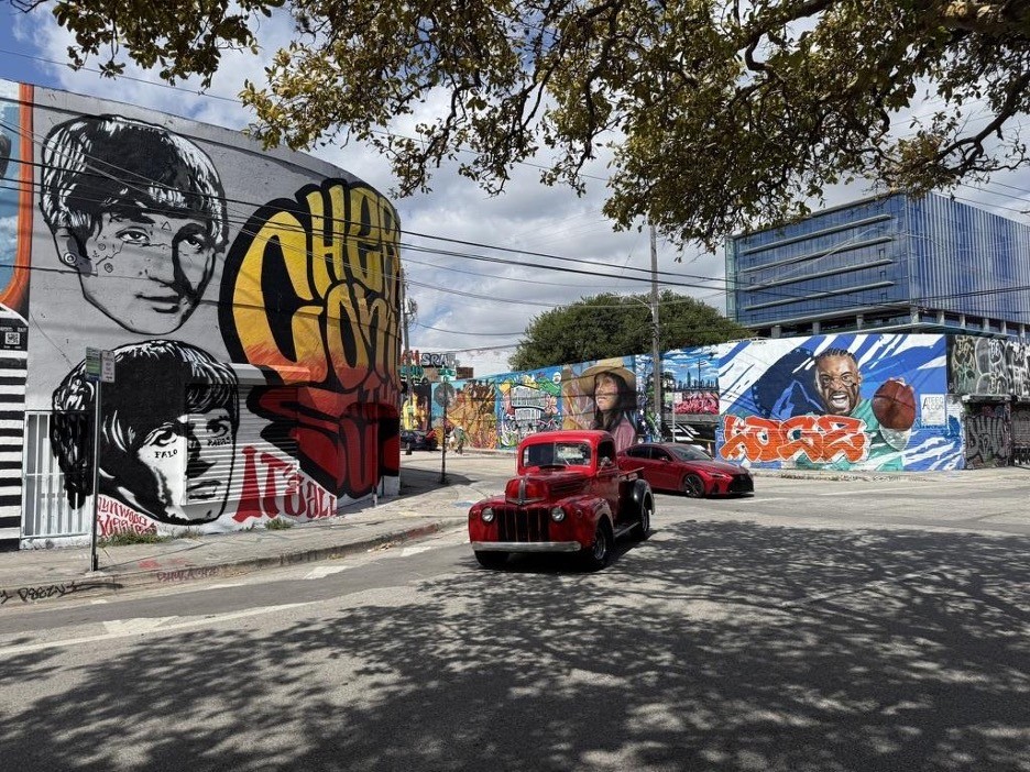 Miami street photo, in front of a painted wall and 2 red cars on the picture