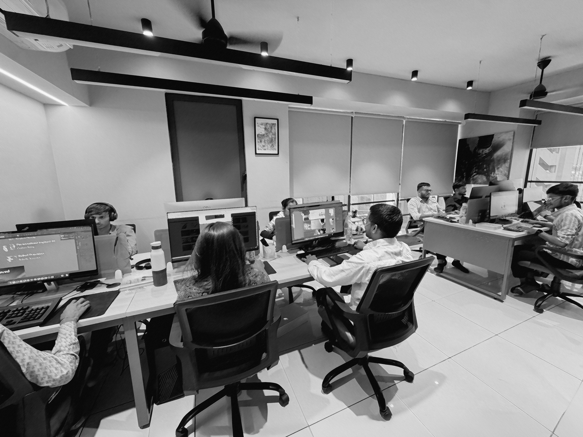 Black and white photo of two people looking at a computer screen with papers on wall