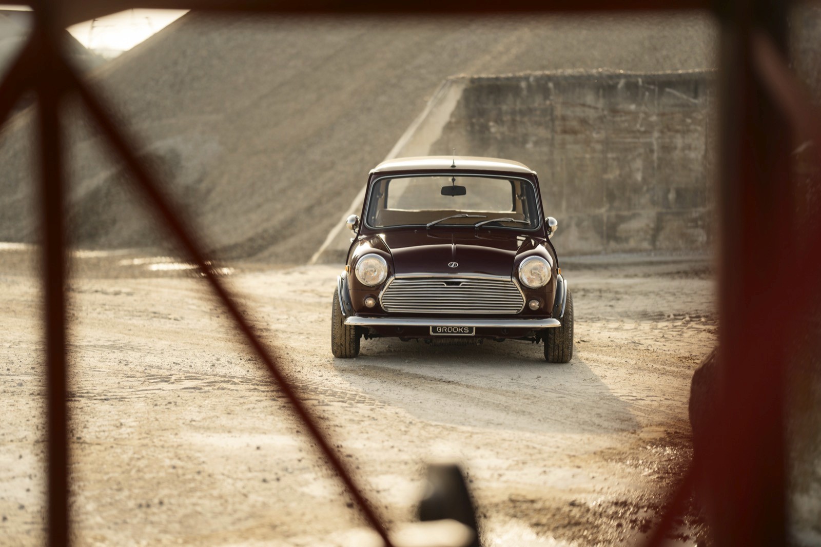 A compact car drives on a sandy surface, framed by geometric structures in the foreground.