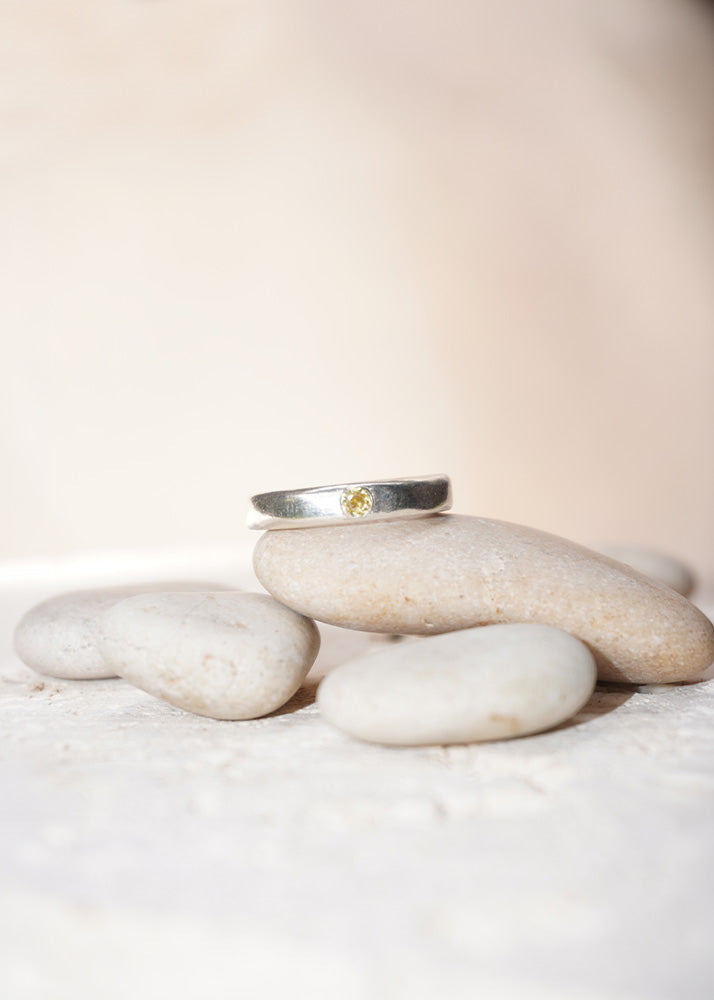 Silver ring with a yellow gemstone on a stack of white stones against a beige background