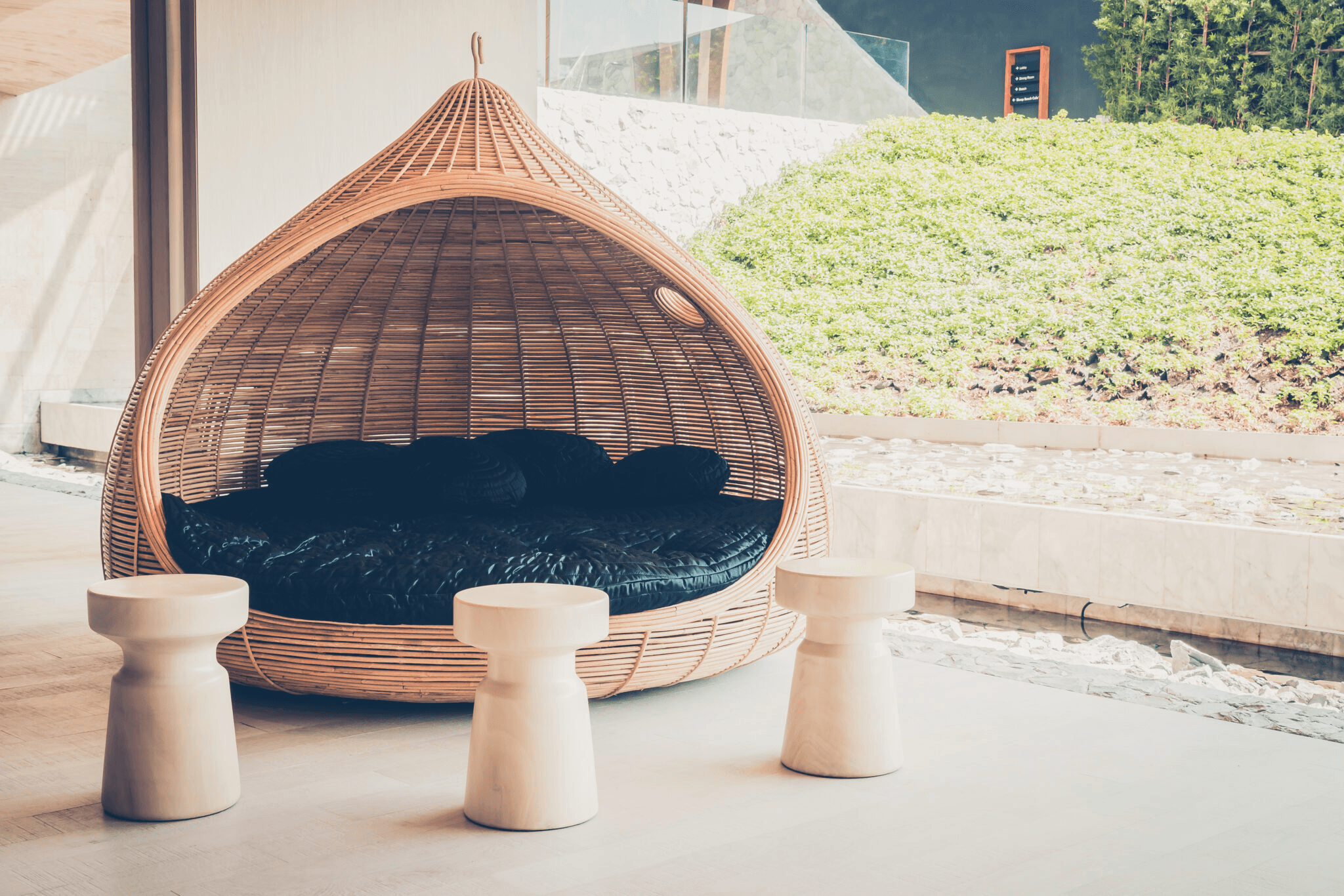 Single-story house with a terracotta-tiled roof, archway entrance, plants in the yard, and a paved driveway. Bright, sunny day, tropical vibe.