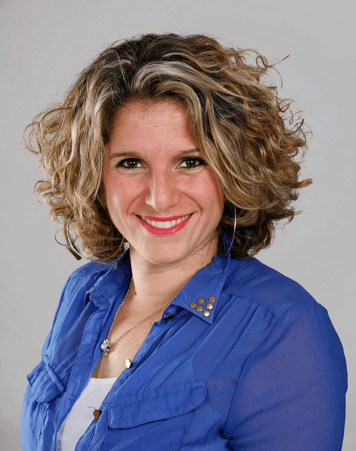 Casual studio portrait of a bearded man with curly hair in a white shirt, arms crossed, on a light gray background.