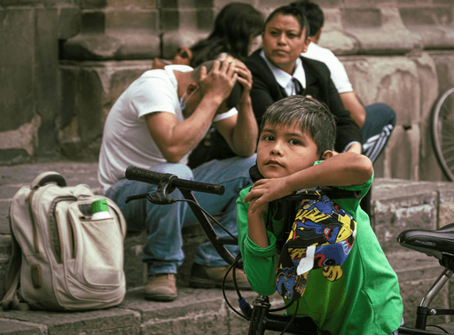 Three children sit on the ground; two appear concerned while one hugs their knees, showcasing vulnerability and emotion.