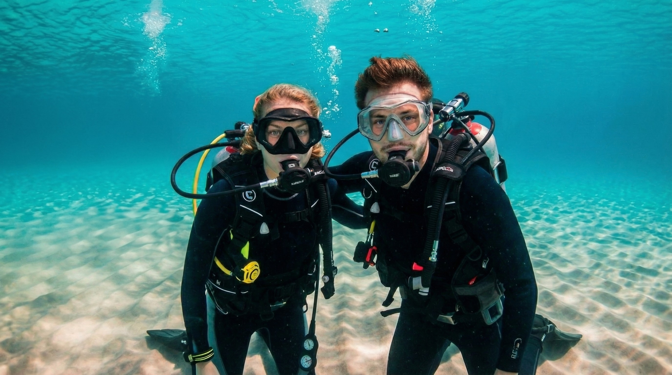Two scuba divers posing together underwater over a sandy ocean floor