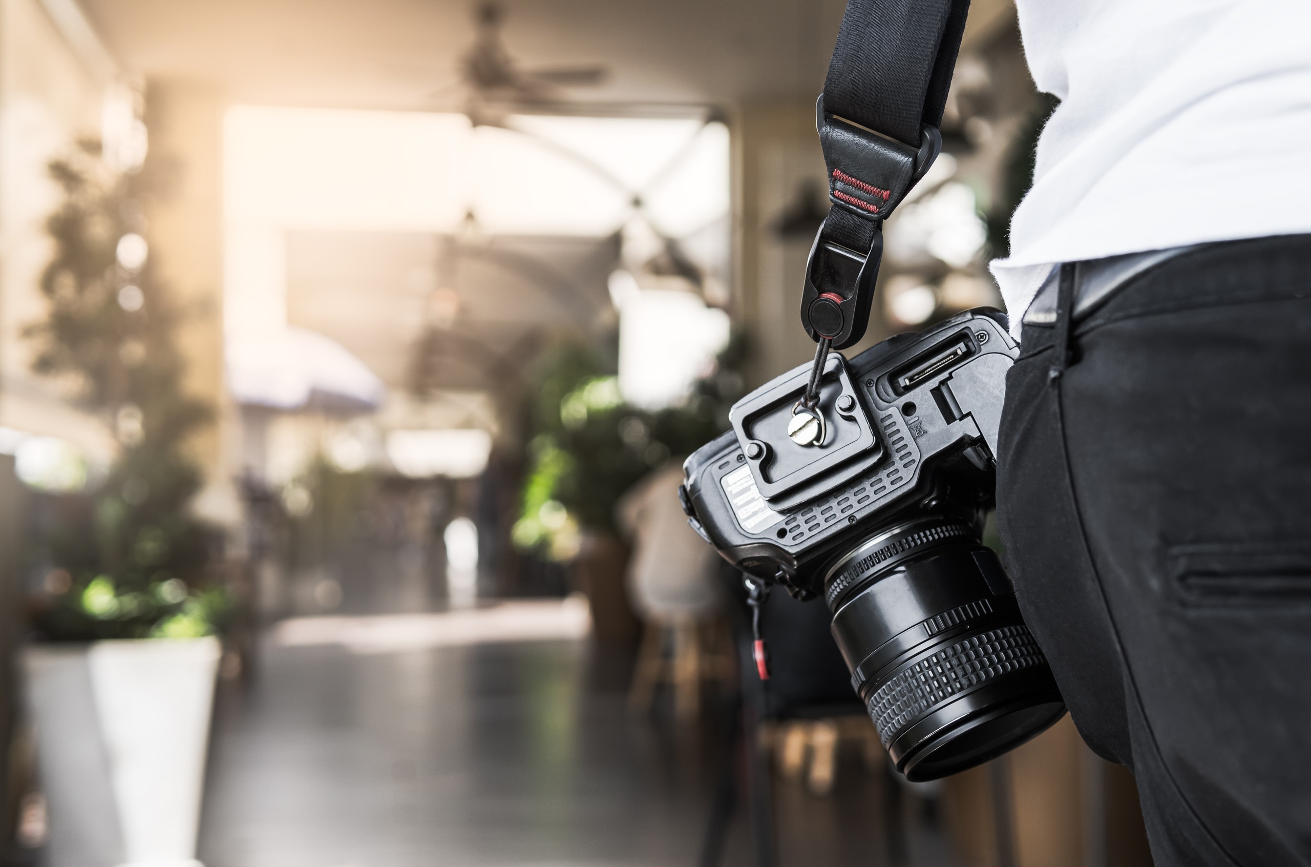 Professional DSLR camera hanging from photographer's shoulder at venue