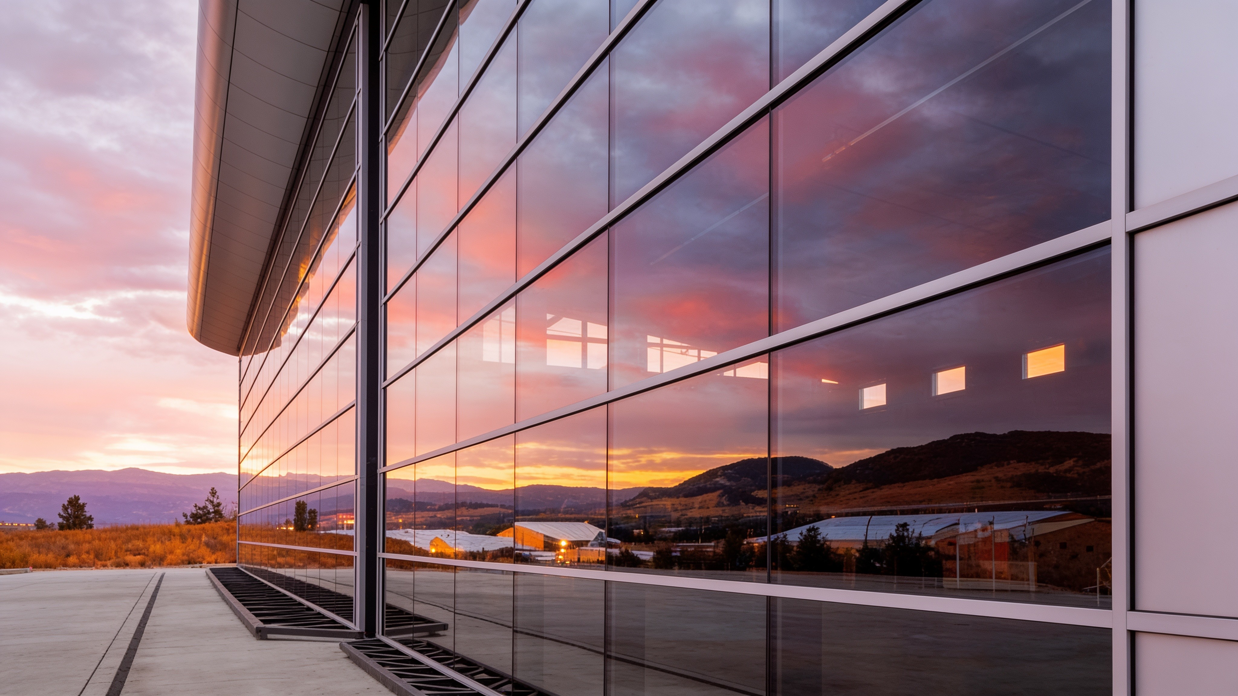 Glass-and-metal aerospace hangar facade reflecting a sunset
