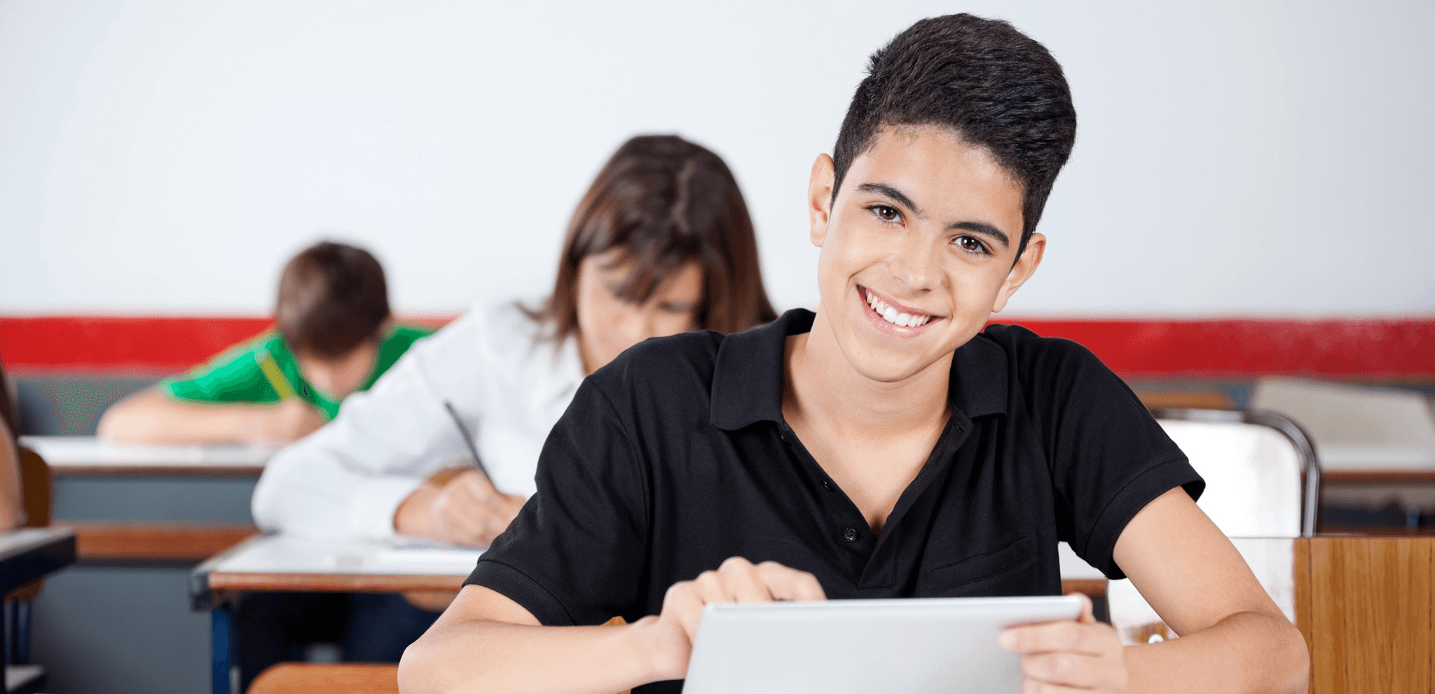 Smiling student holding a book while sitting by a desk in classroom and studying | Let Me Learn