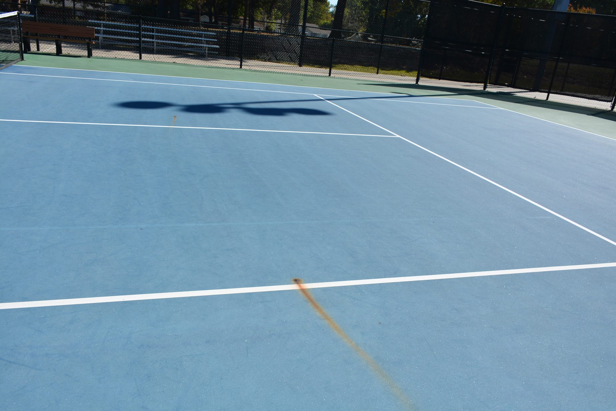 Faded light blue court with a rust stain before resurfacing at Conway Tennis Center in Conway, AR
