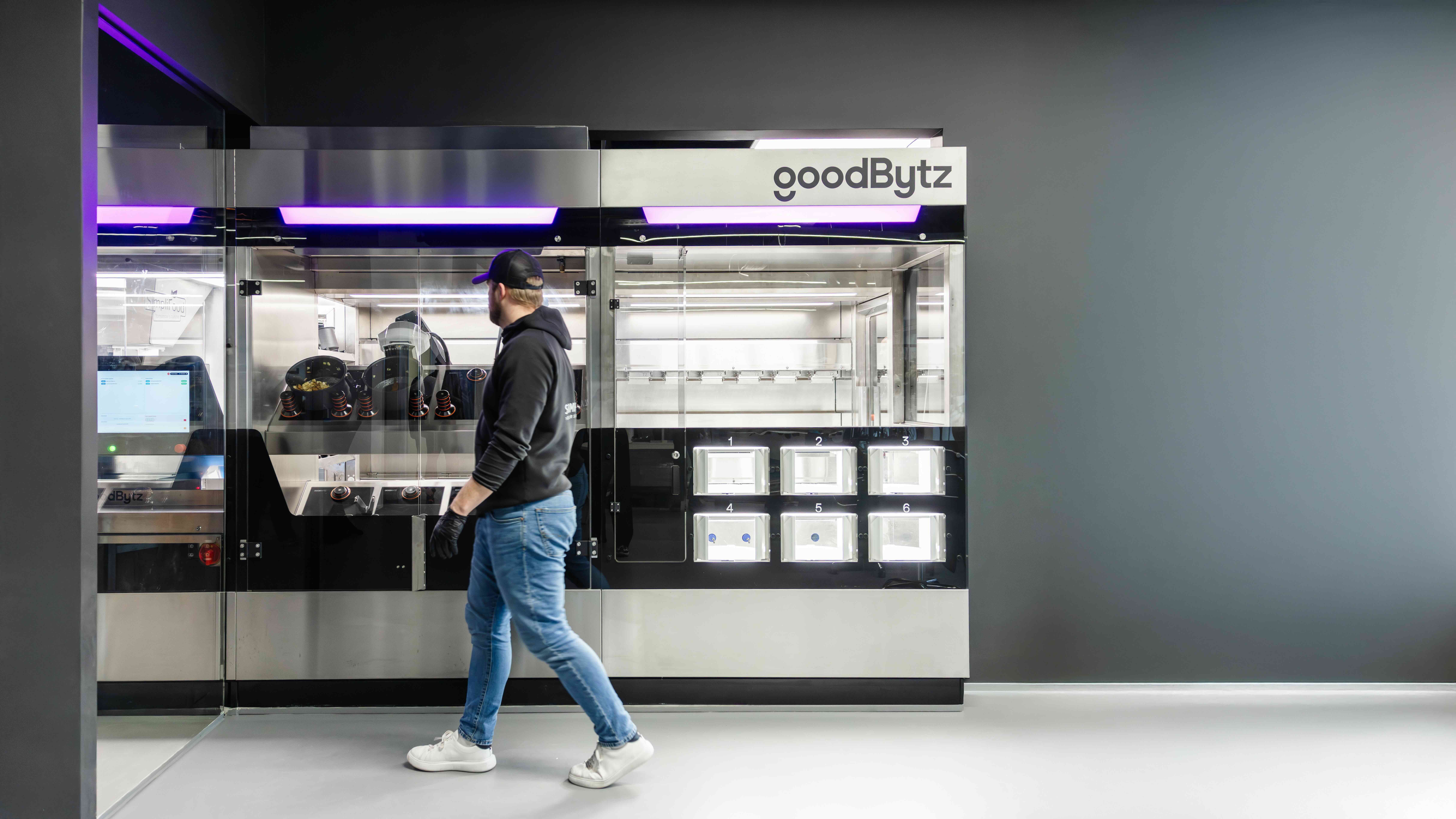 A person stands at a modern kitchen robot in a sleek, minimalist setting with neutral colors.