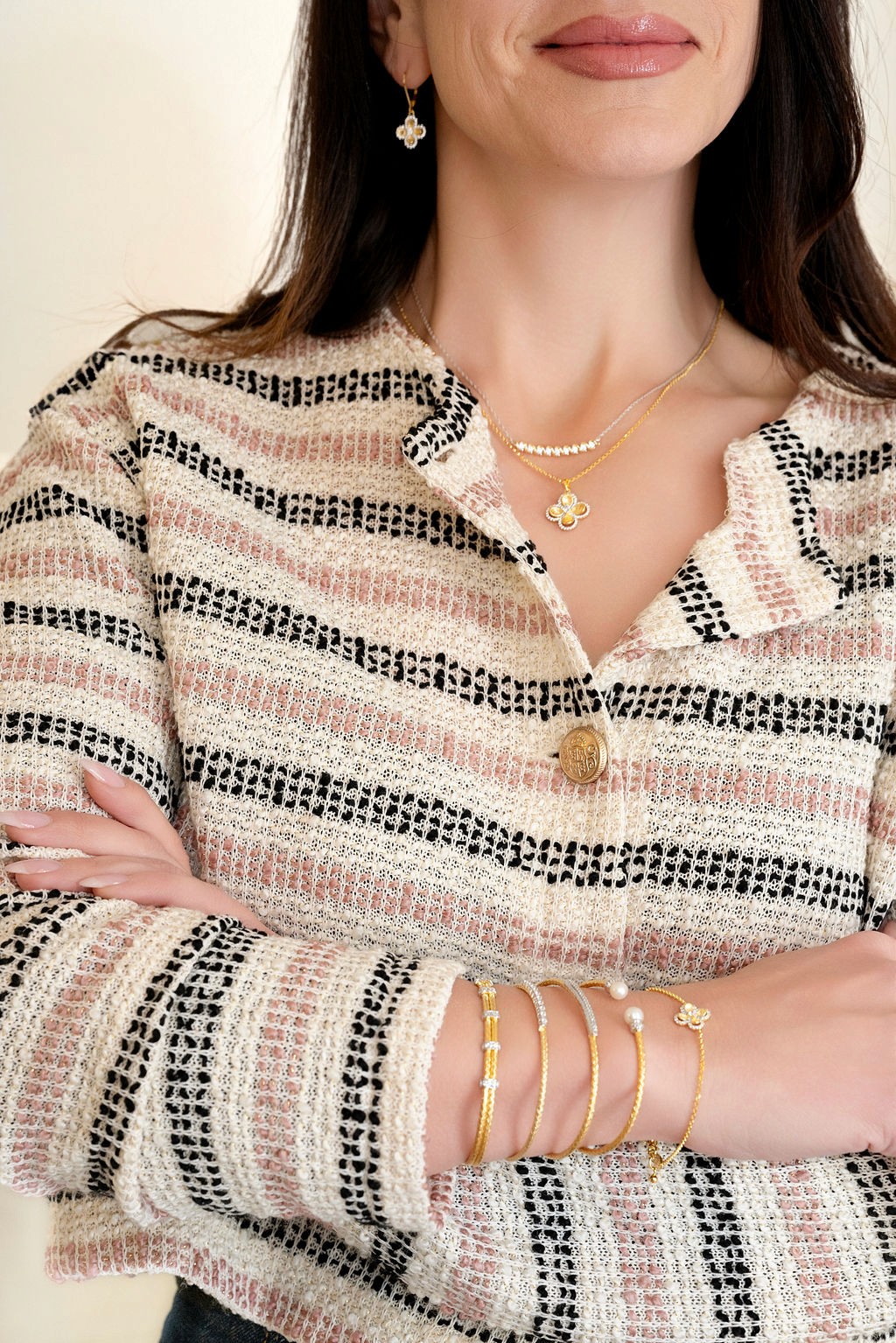 photo of female model with arms crossed and knitted long sleeve top, showcasing a variety of gold bracelets and necklaces. 