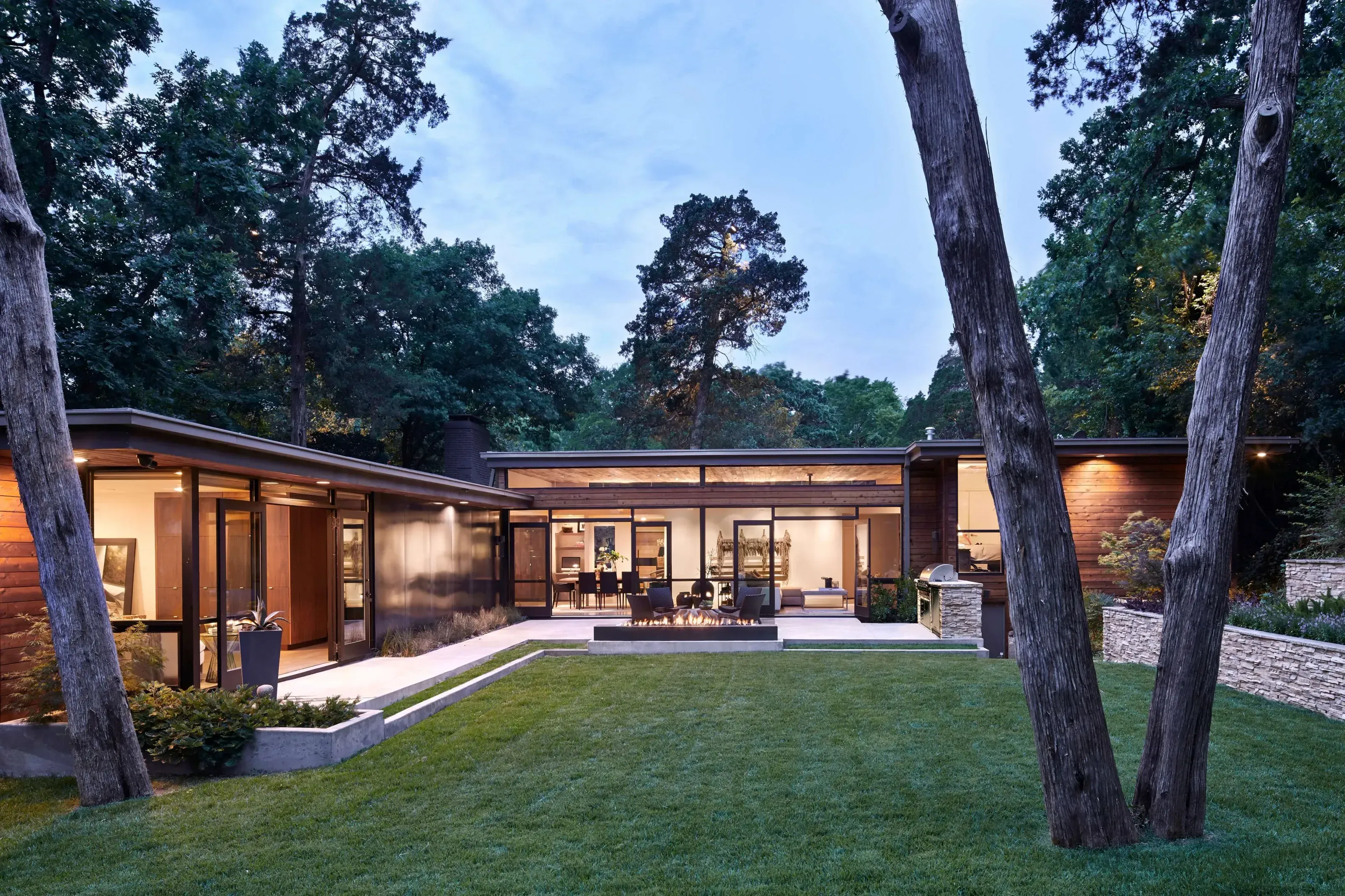 Evening exterior of flat roof modern home in Kessler Park with custom fire feature and lawn