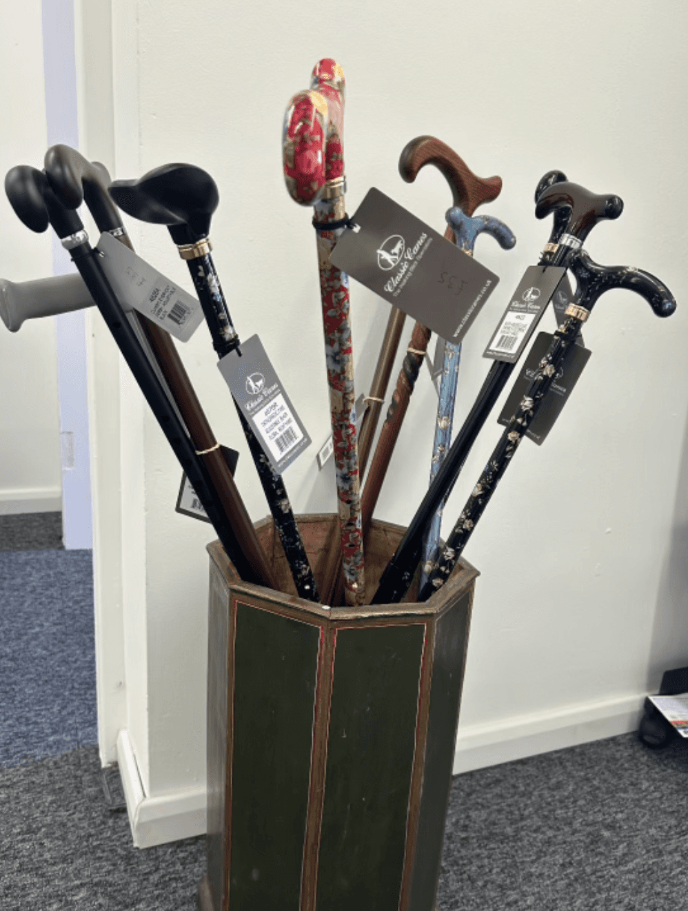 Image shows a cane stand filled with different types of walking sticks and canes. There are plain ones and ones with colurful handles and designs.