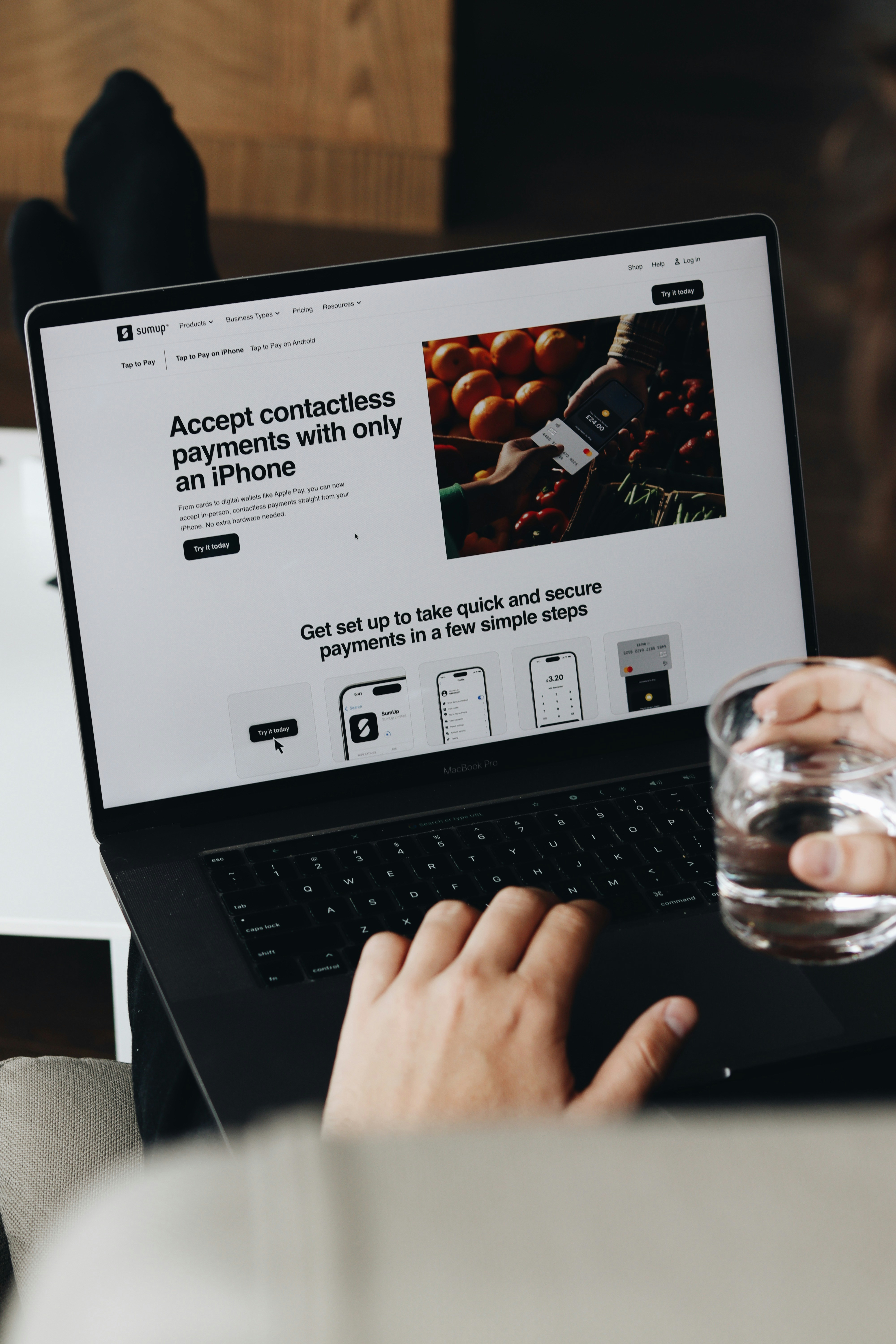 someone using a laptop to build a website whilst holding a glass or water