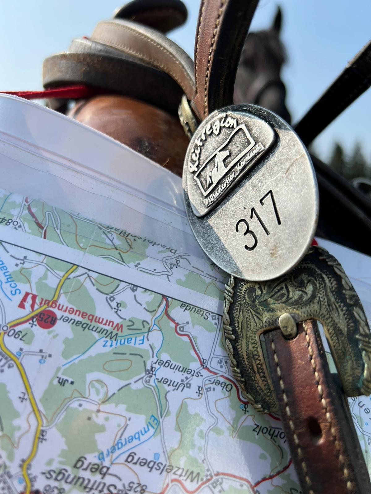 Smiling young woman with long hair standing against a dark green background, holding a finger to her chin.