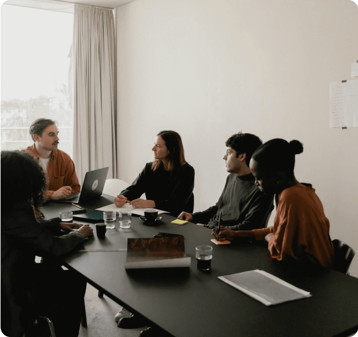 Team members engaged in discussion around a conference table in a meeting room.