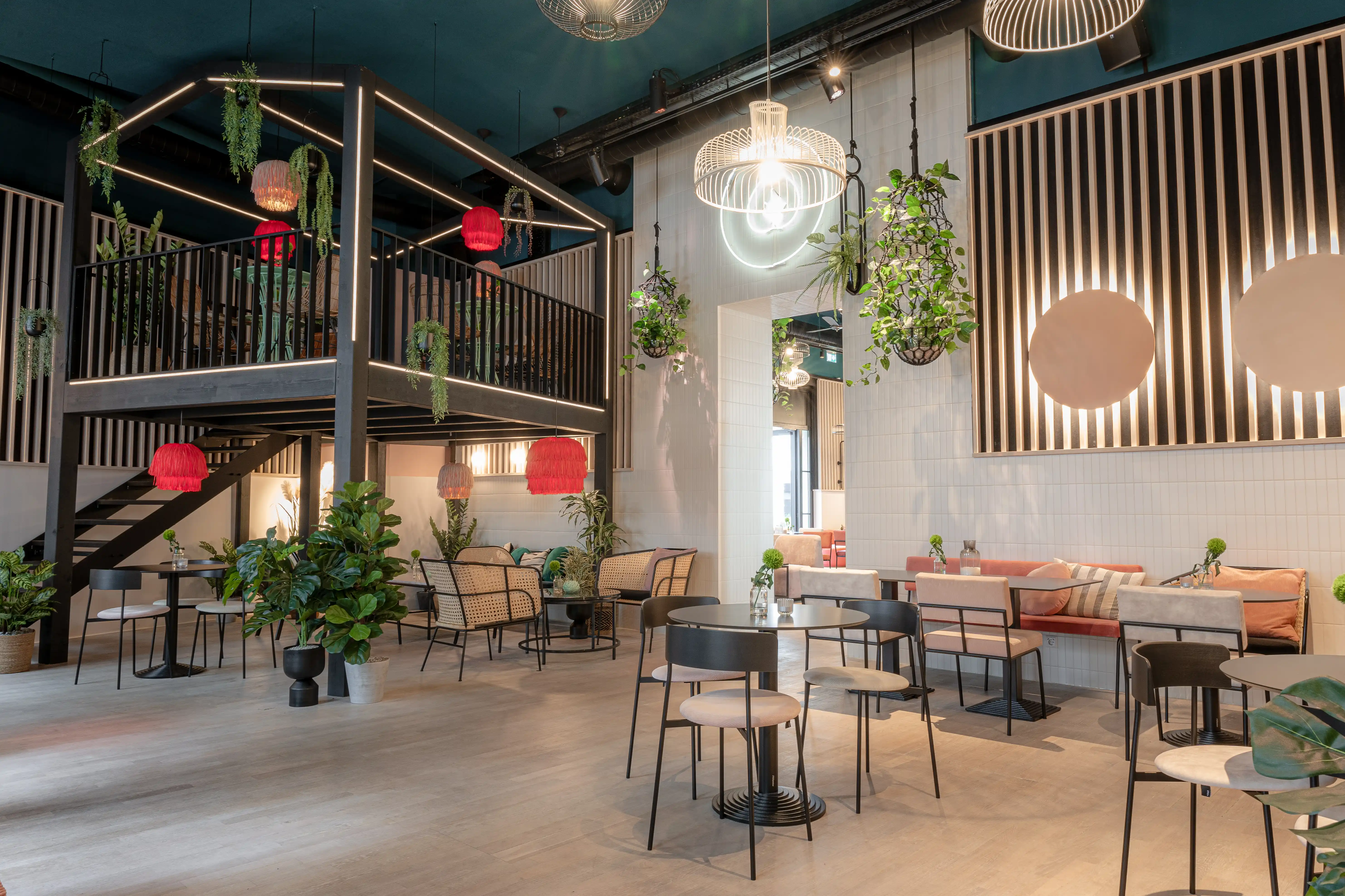 Main room at LOKAL VIER with a black steel mezzanine with light lines, red fringe lamps, copper wall circles, plants and mixed black and rattan seating.