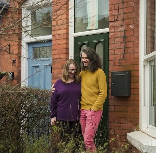 A couple laughing outside the front of their house.