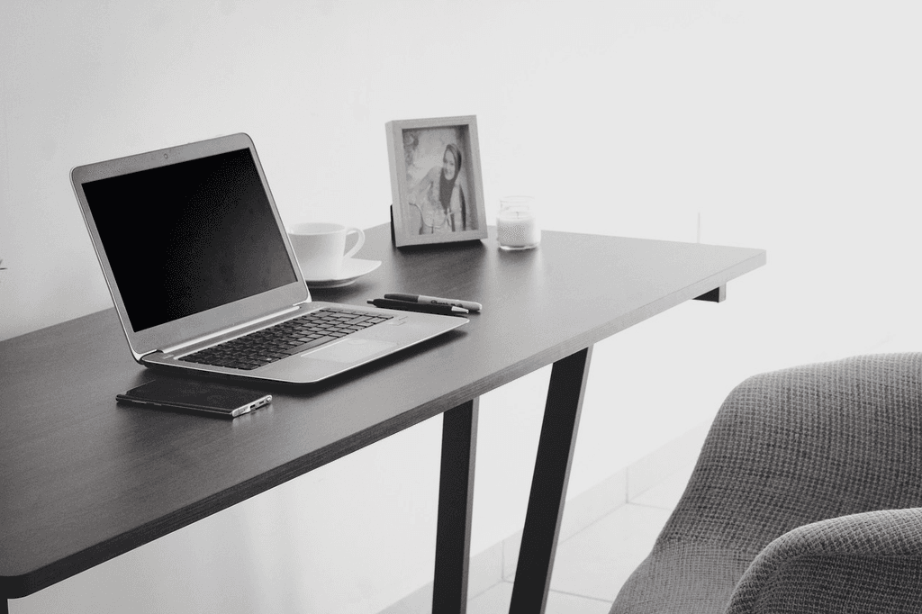 Home office desk set-up, with a laptop, phone, and photo on top and a chair to the side.