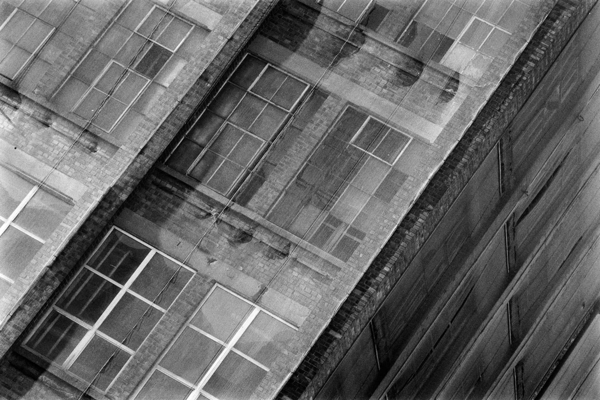Oblique view of warehouse wall with protective netting covering weathered surface, geometric grid pattern of netting creating rectangular divisions across industrial brick building
