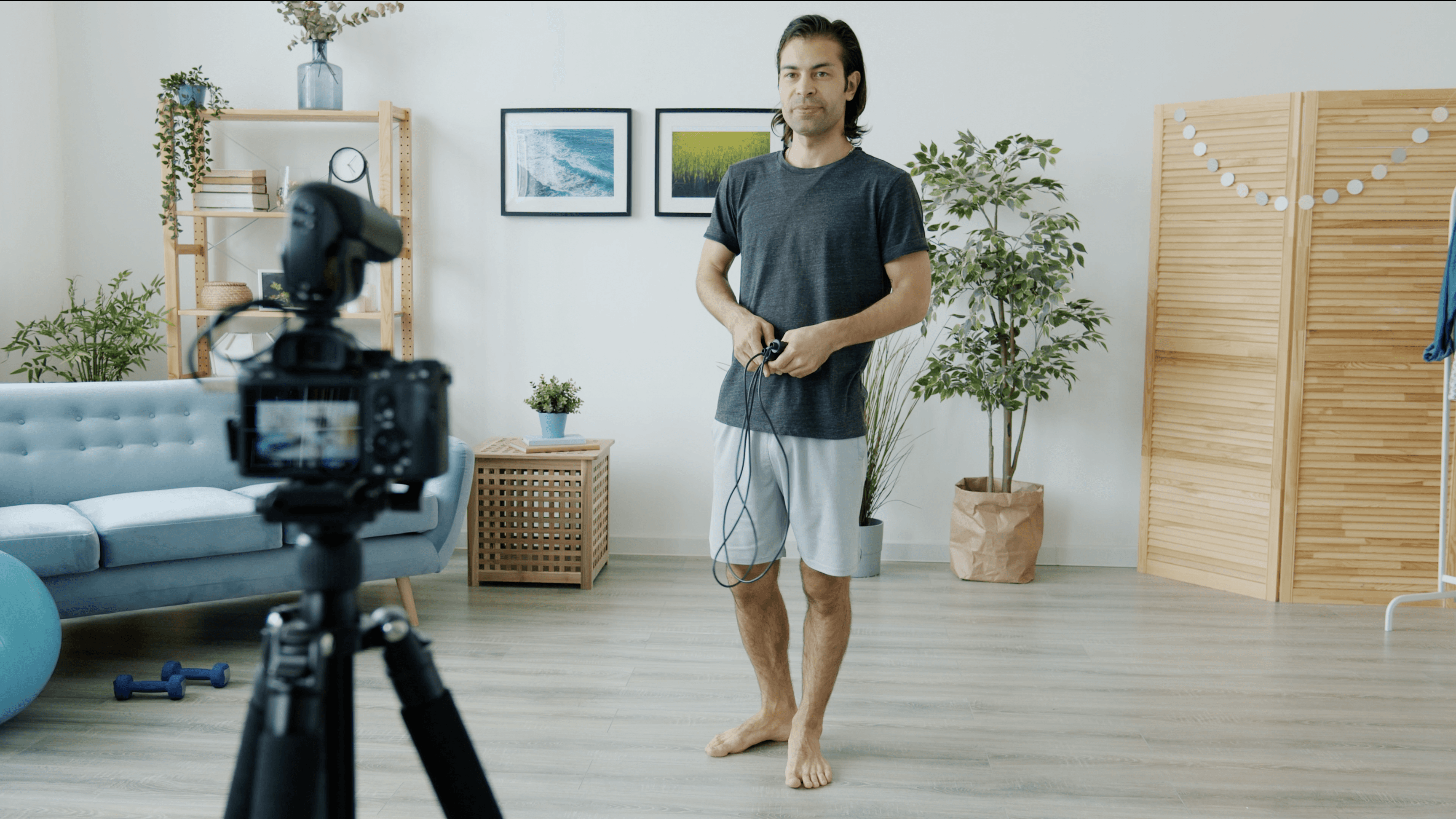 Male creator filming a home workout tutorial, standing in front of a camera on tripod in a bright home studio
