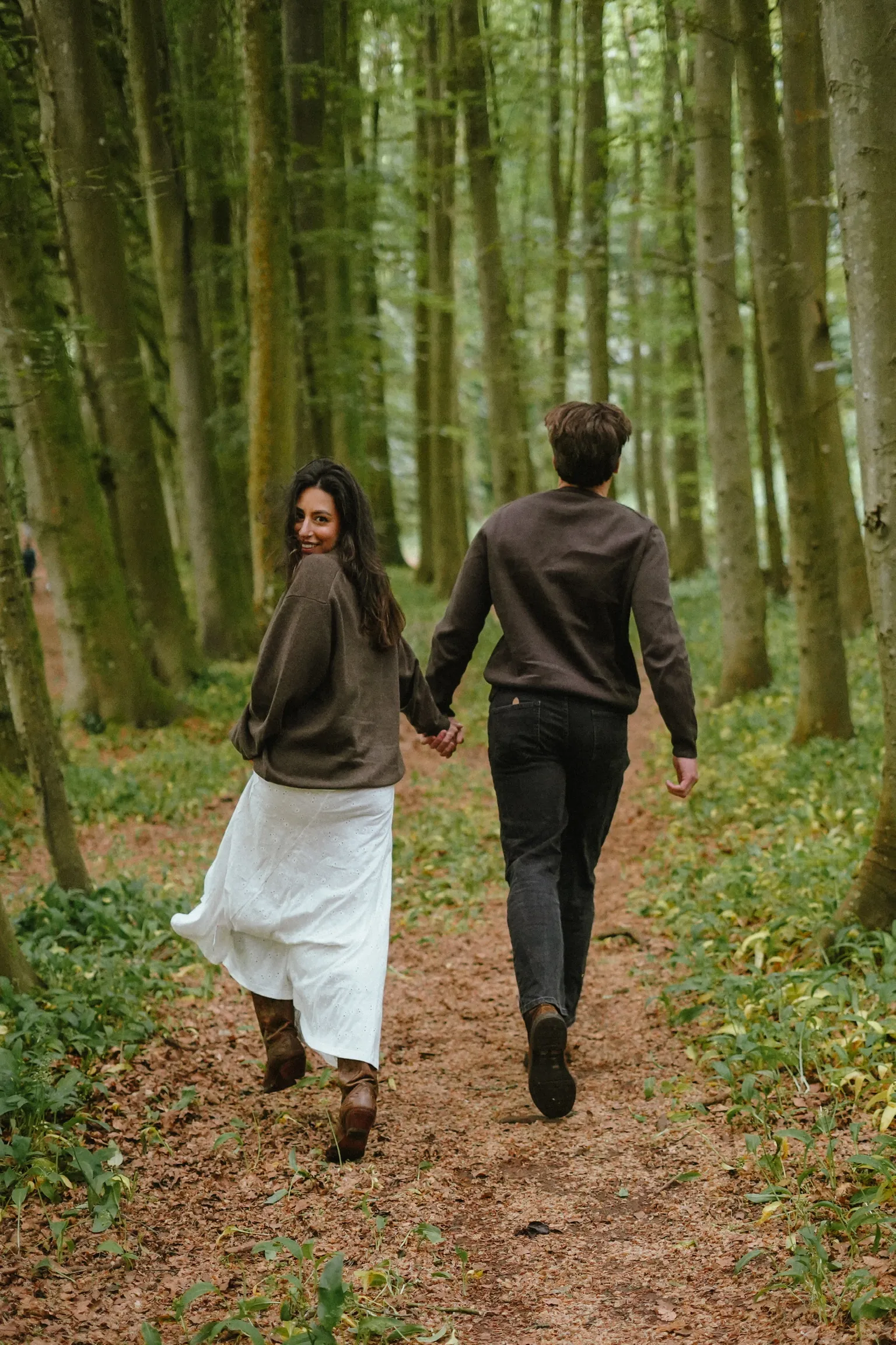 Connor and Cherine walking hand in hand through a green woodland