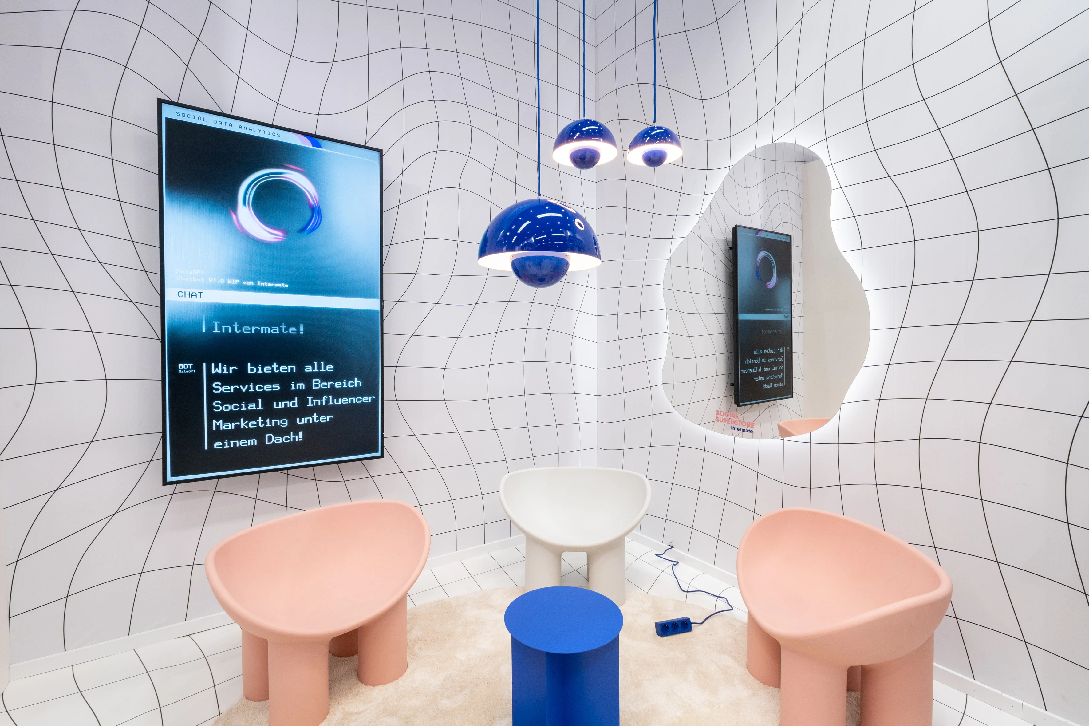 Surreal lounge niche with warped grid walls, pink chairs, blue pendant lamps and organic mirror at the Intermate booth.