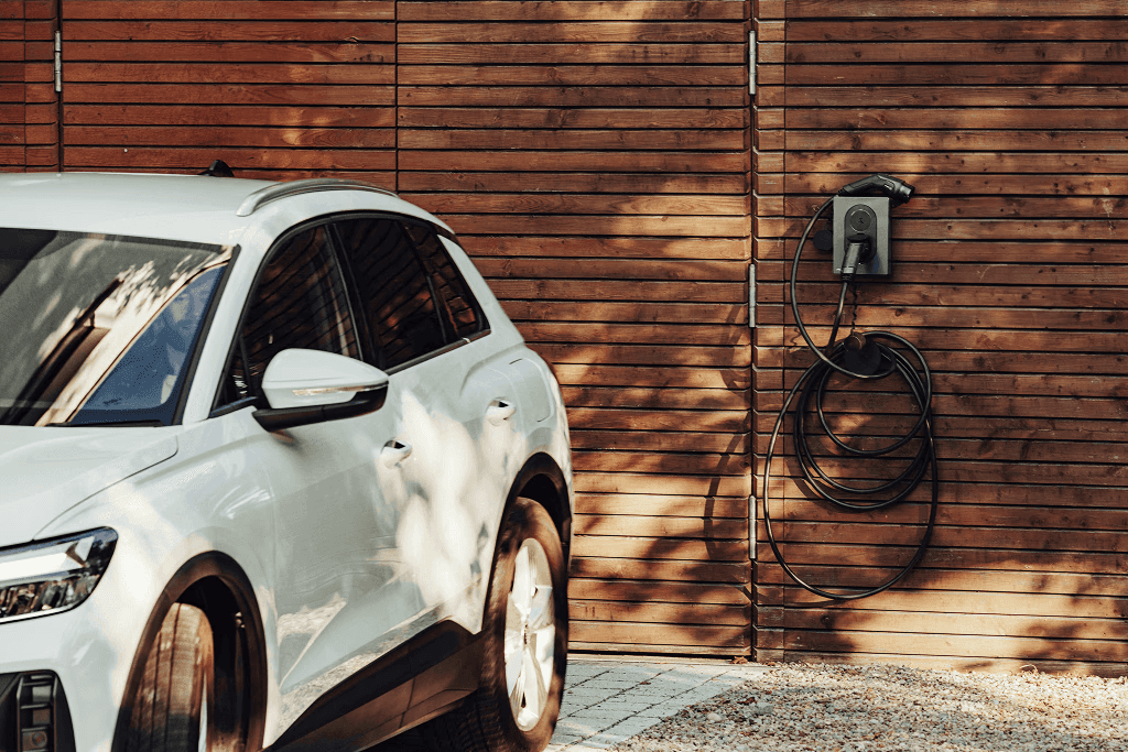White Electric Vehicle plugged into an EV charger mounted on the wood panneled wall of a home