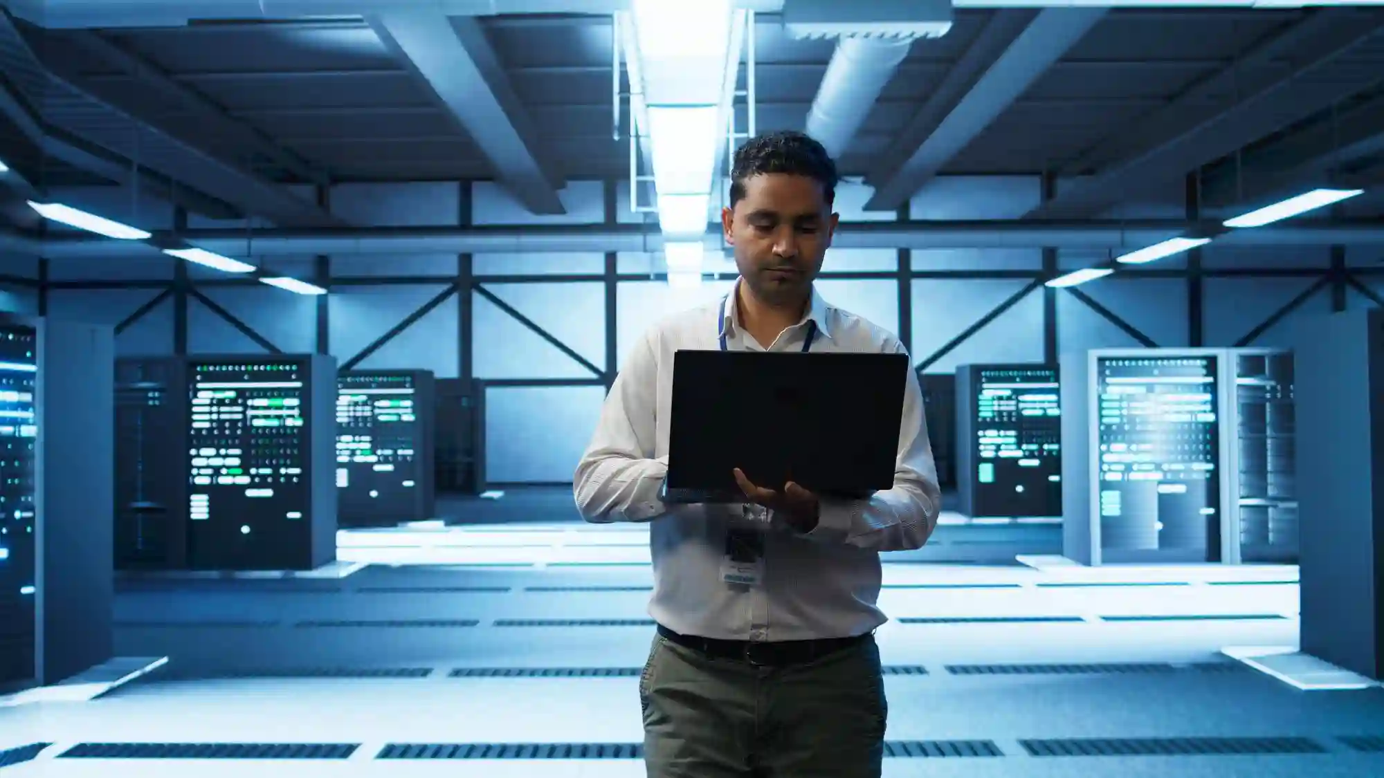 An IT professional monitoring servers with a laptop, symbolizing the active defense of data centers against persistent cyber threats.