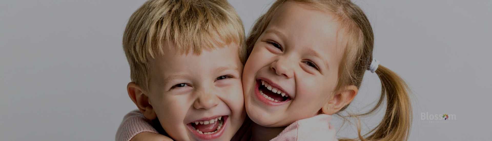 Two young children, a boy in a blue sweater and a girl in pink, hug and smile joyfully. 