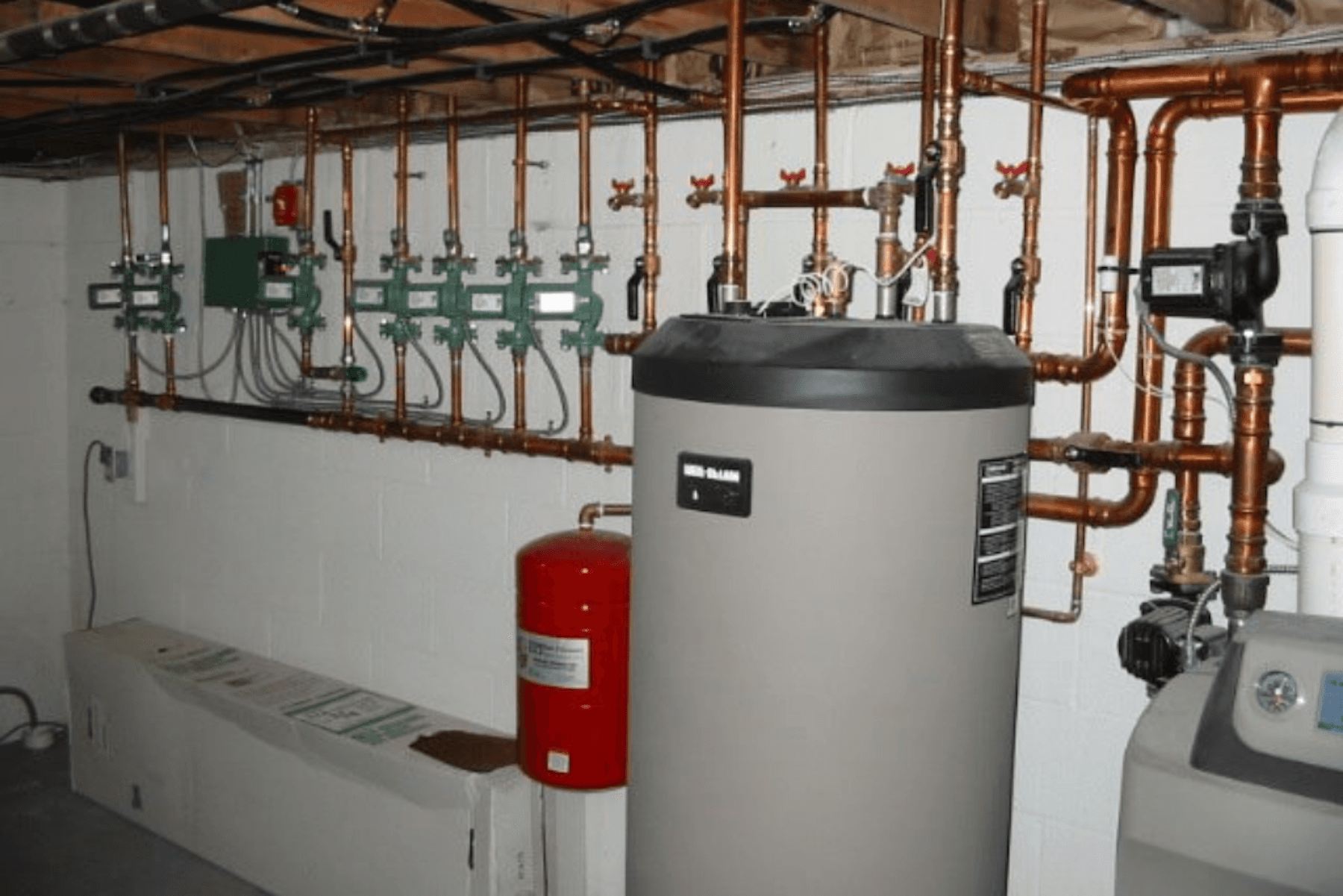 Professional plumbing and heating installation with water heater, copper piping, valves, and organized mechanical system layout.