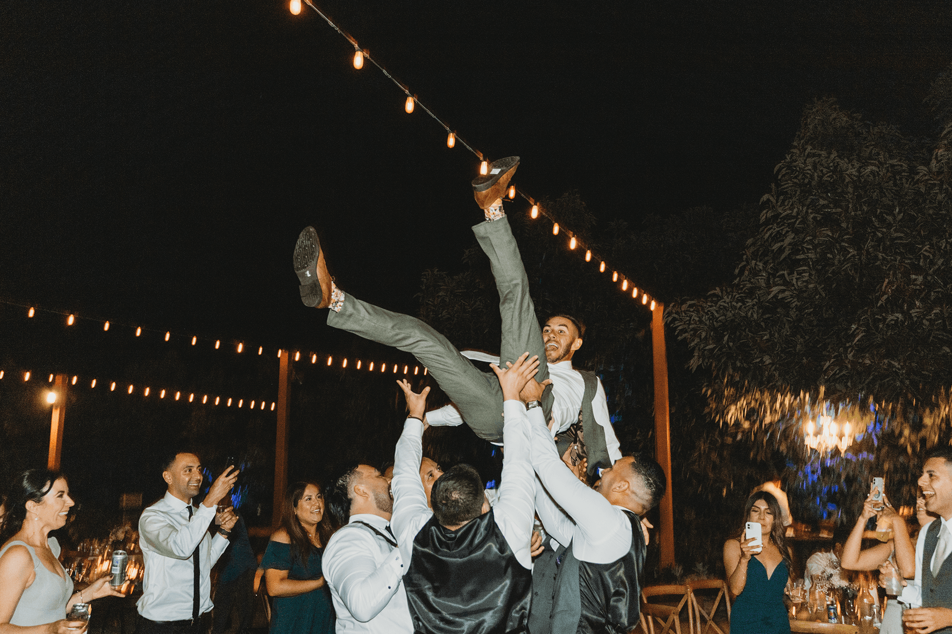 Groomsmen lifting groom in the air during reception