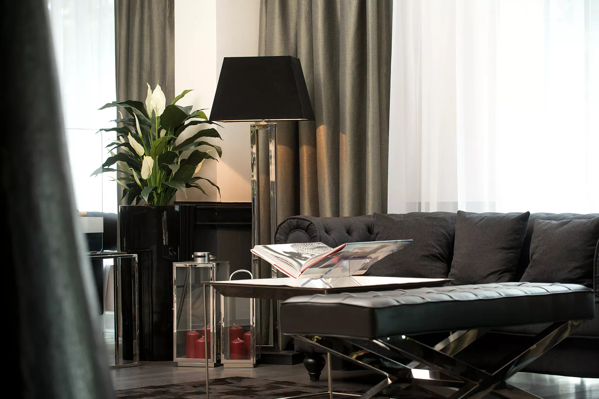 Aufnahme des Loungebereichs bei der Rezeption mit Sofa im Hintergrund, Tisch mit Magazin und einer gemütlichen Stehlampe