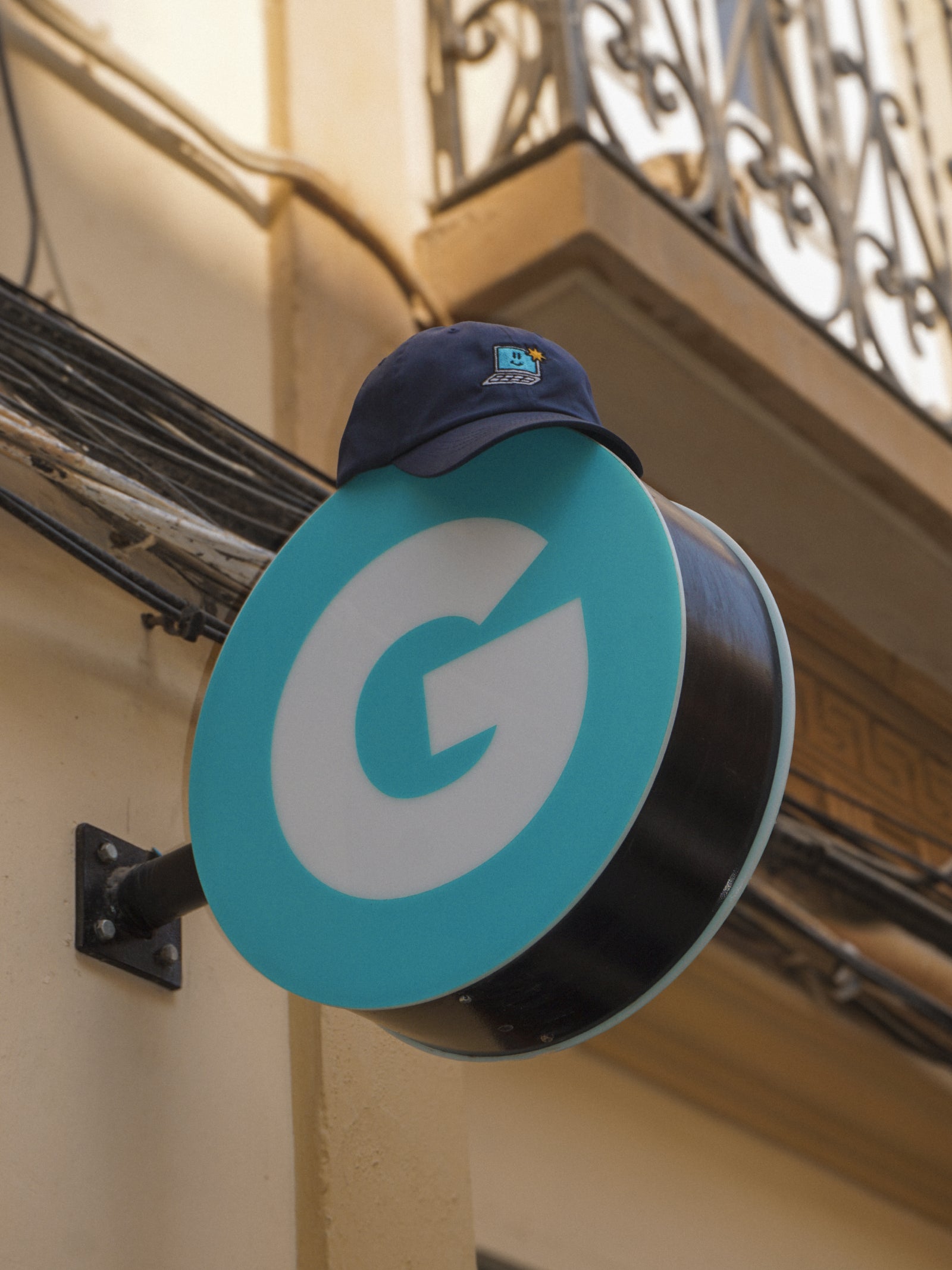Teal sign with a large white 'G' on a building exterior and a navy cap on top