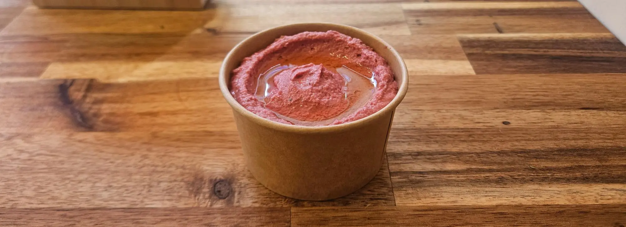 Pot kraft de houmous  couleur rose garni d’un filet d’huile d’olive