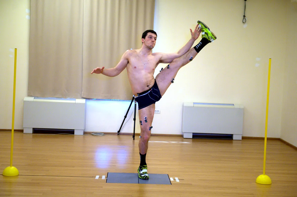 Goalkeeper with EMG sensors and motion capture markers doing a high leg swing on a force plate