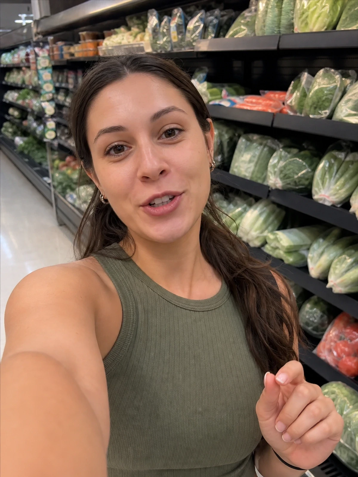 UGC-style photo: outdoor lifestyle creator, in a grocery aisle, holding a phone at arm's length while talking to camera, mirror-style vertical shot.