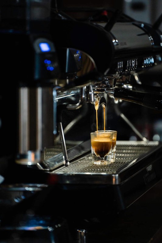 A plate of five savory soft-shell tacos, generously filled with seasoned meat, cilantro, and shredded cheese, presented in a dimly lit, atmospheric setting with a lit candle and a copper vessel in the background.