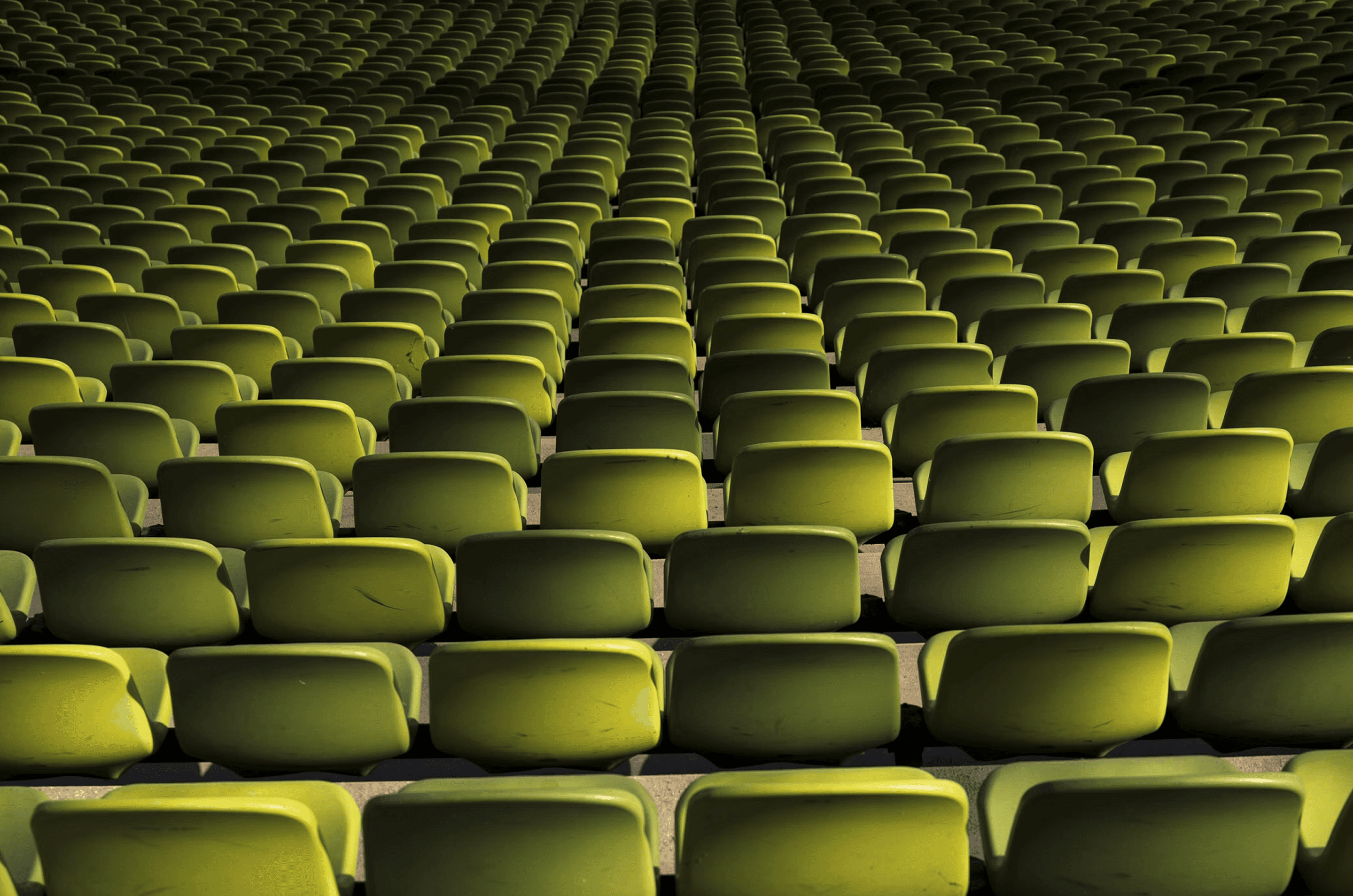 Rows of empty green stadium seats viewed from above, forming a repeating pattern — representing scale, audience reach, and how strong B2B brand impact is built by engaging the right accounts at scale rather than everyone at once.