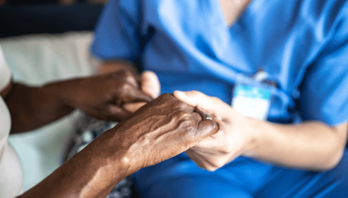 Caregiver gently holding an elderly person’s hands.