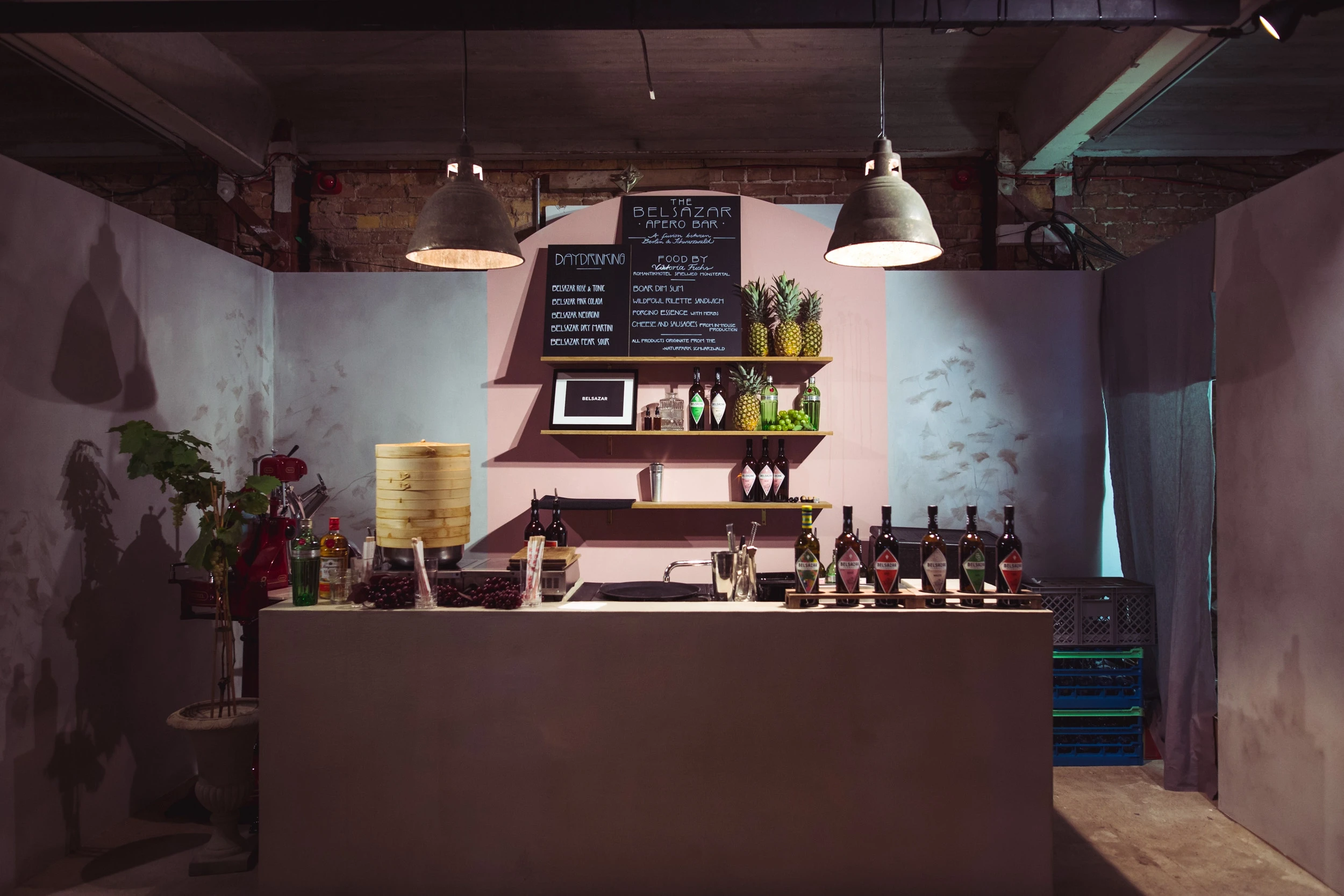 Belsazar apéro bar at DIAGEO BCB18 with a pink wall panel, chalkboard menus, brass shelves with pineapples and bottles on a concrete counter.