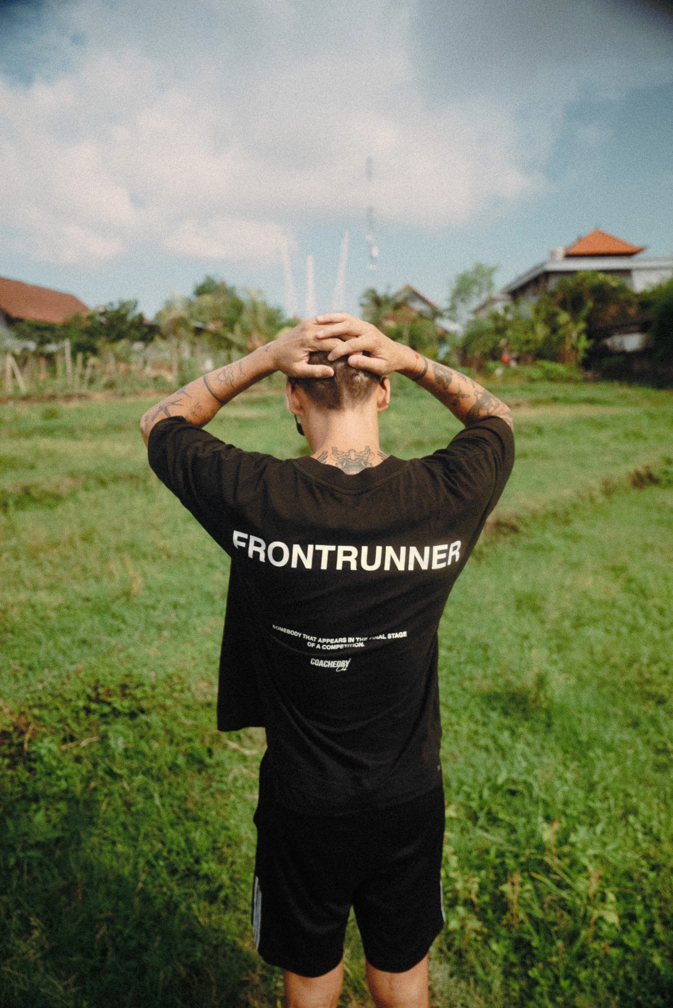 Man standing outdoors with hands behind his head wearing a Frontrunner branded shirt.