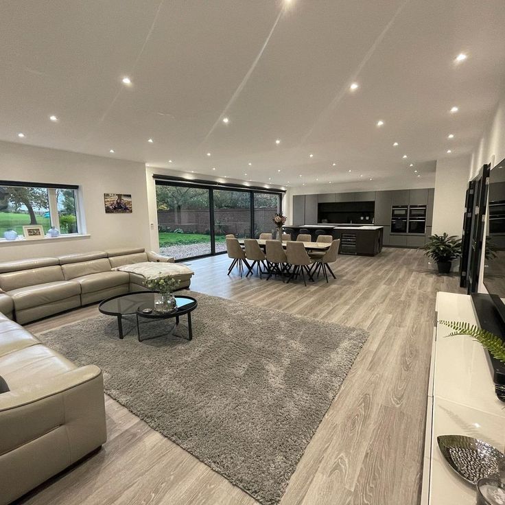 Modern glass and wood cabin with a cozy outdoor deck featuring wicker furniture, surrounded by lush green trees and a serene forest setting.