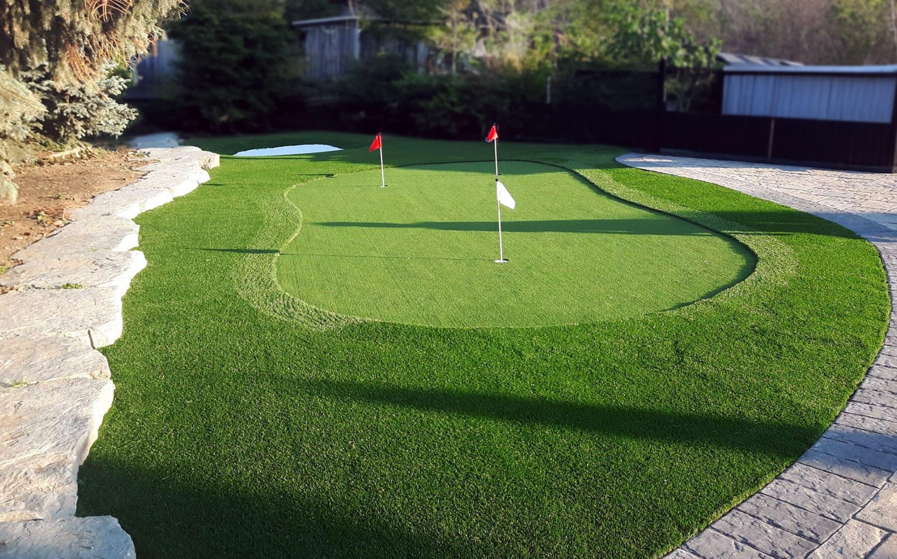 A backyard featuring Kent Fringe grass surrounding Golf Leisure putting turf by AGL Grass North.