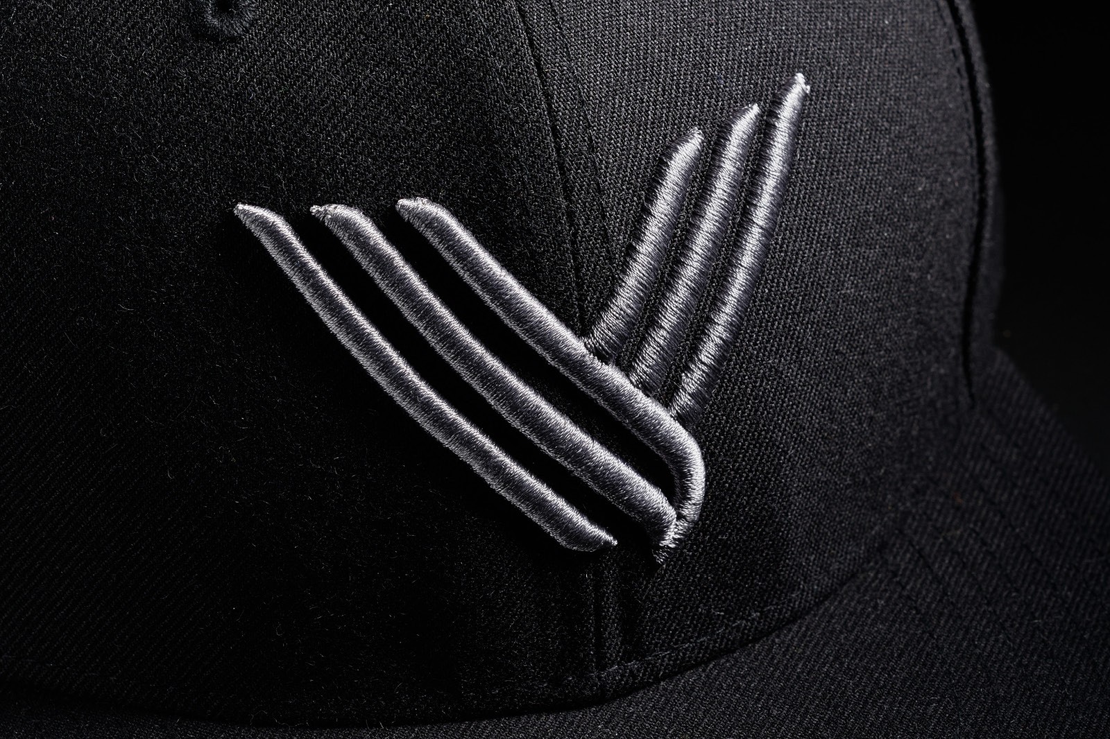 Close-up of a black cap featuring a stylized three-stripe logo in gray.