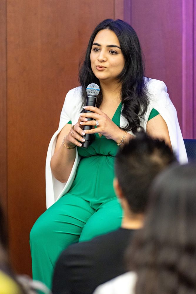 Karishma speaking with a microphone on a panel stage