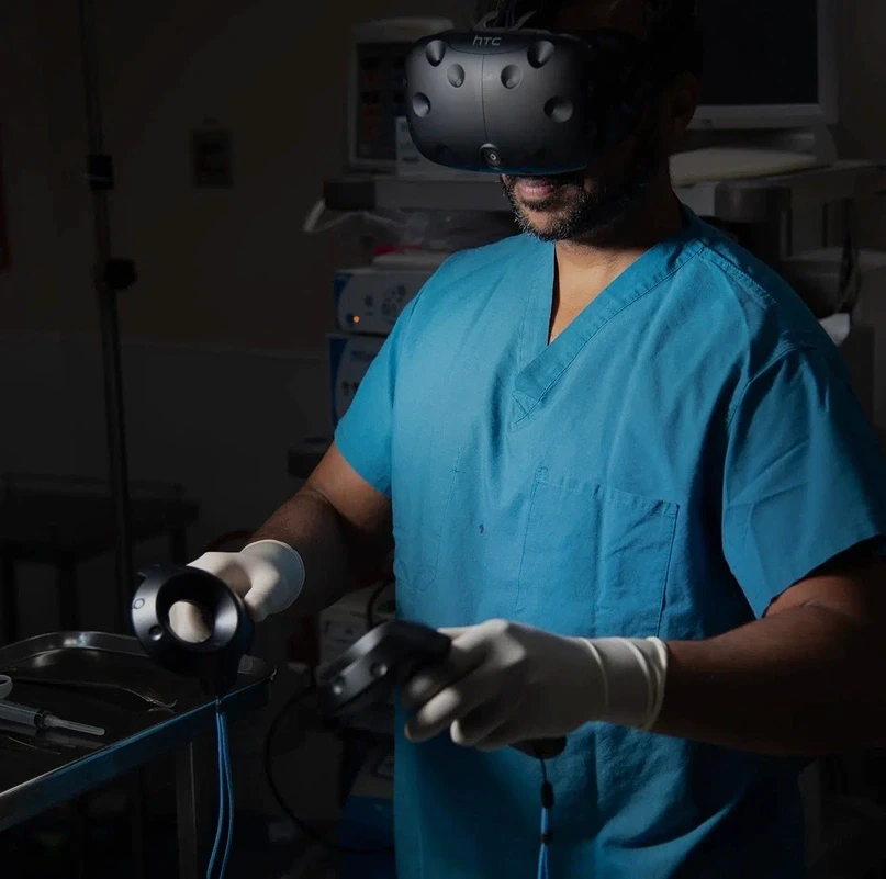 Medical professional in scrubs using an HTC Vive VR headset and motion controllers in a clinical setting