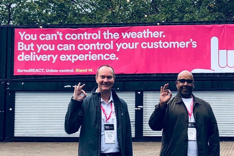Two men posing in front of Sorted delivery banner at event
