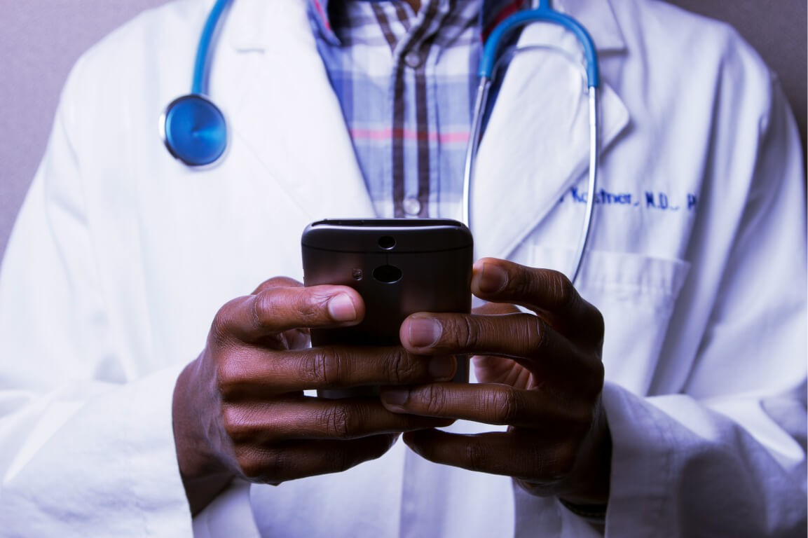 Doctor typing on mobile phone wearing white coat wearing stethoscope and dress shirt